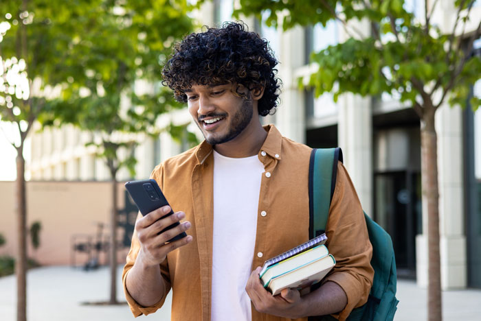 Student outside carrying books and making a call on their cell phone.