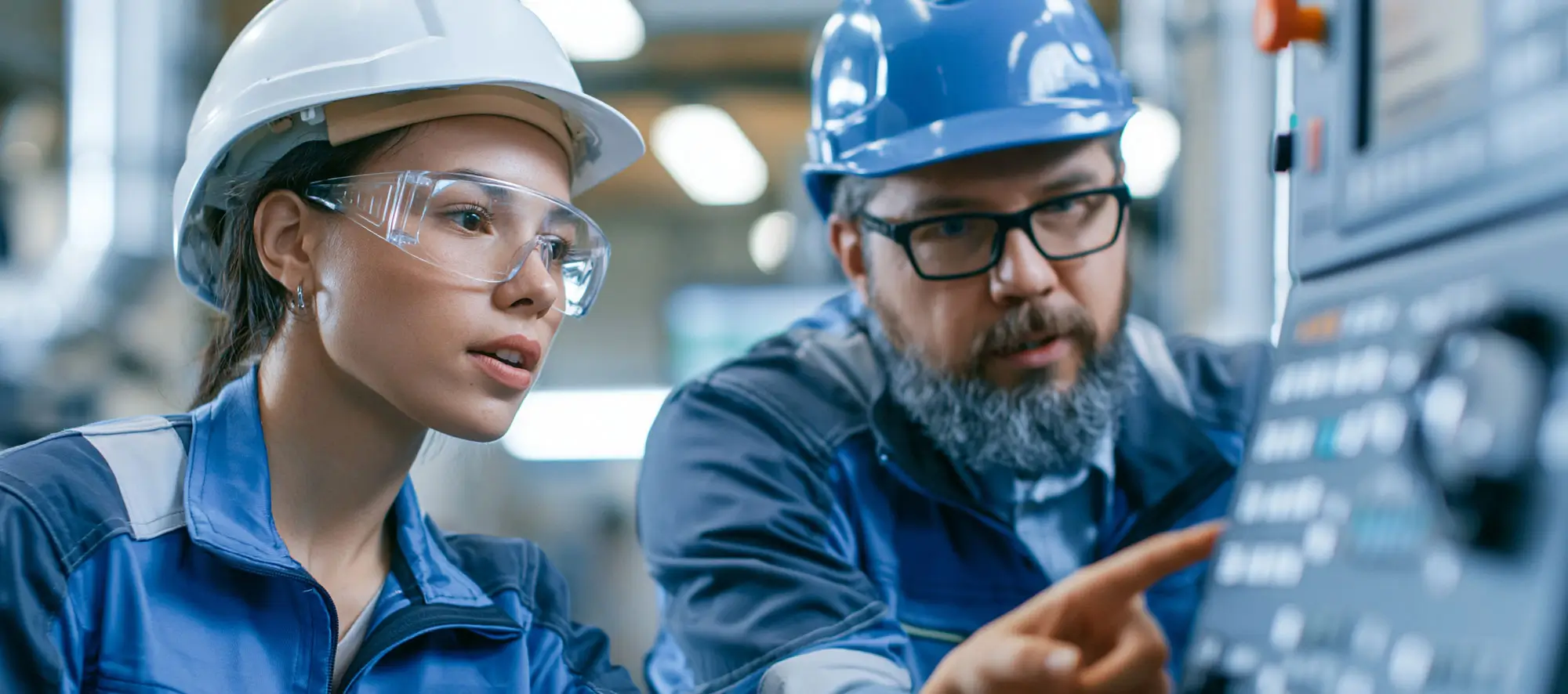 Engineer training female apprentice to use CNC machine in factory.