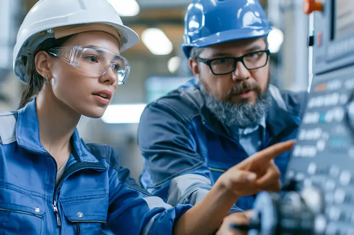 Engineer training female apprentice to use CNC machine in factory.