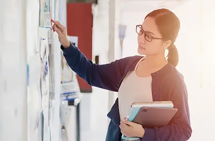 Woman with glasses getting flier from bulletin board.