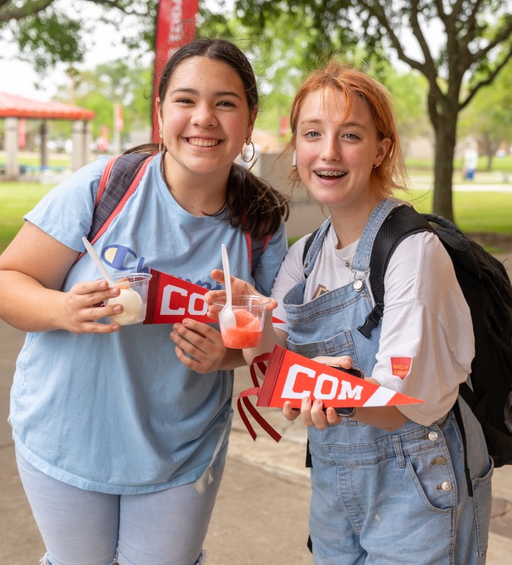 Two students outside with COM pennant flags